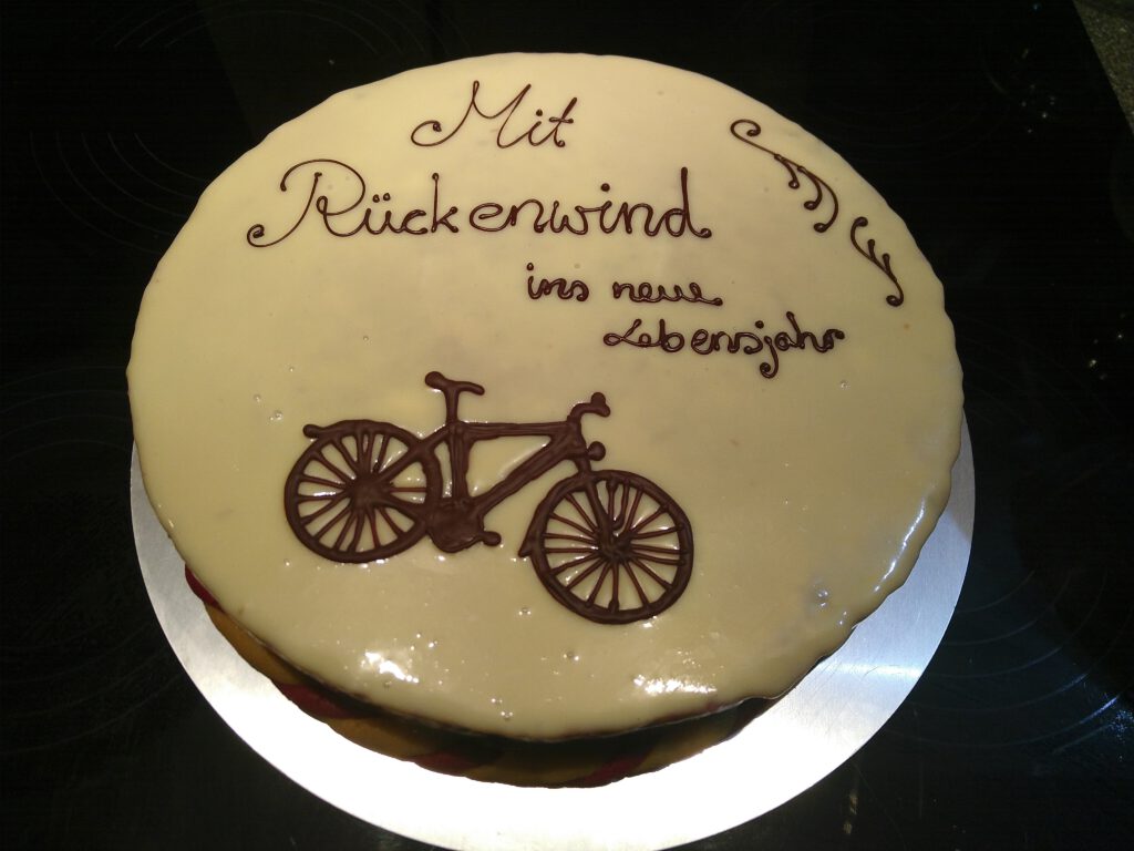 Geburtstagstorte mit Fahrrad aus Schokolade und der Aufschrift „Mit Rückenwind ins neue Lebensjahr“