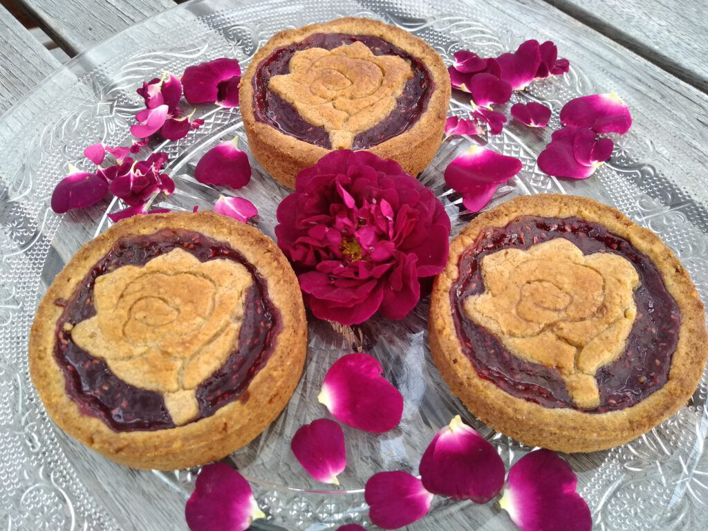 Rosenblüten-Gewürztartes mit einer Rose aus Teig, umgeben von Rosenblättern